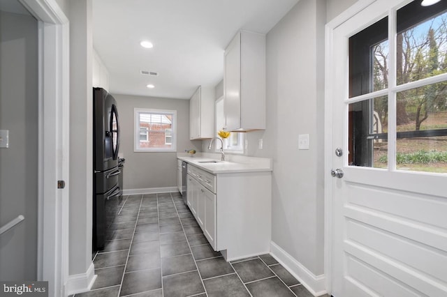 kitchen with dishwasher, black refrigerator, sink, dark tile patterned floors, and white cabinetry