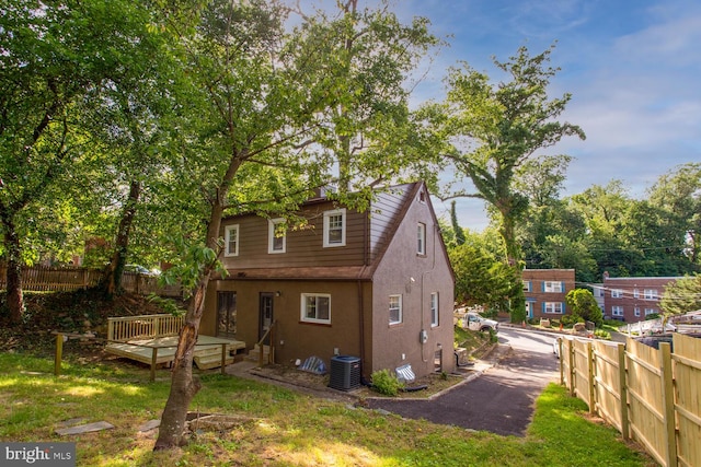 back of house featuring central air condition unit, a wooden deck, and a lawn