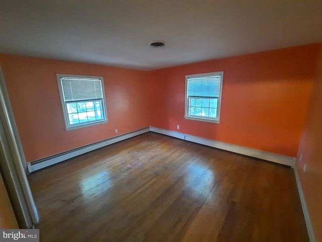 empty room with hardwood / wood-style flooring, plenty of natural light, and a baseboard heating unit