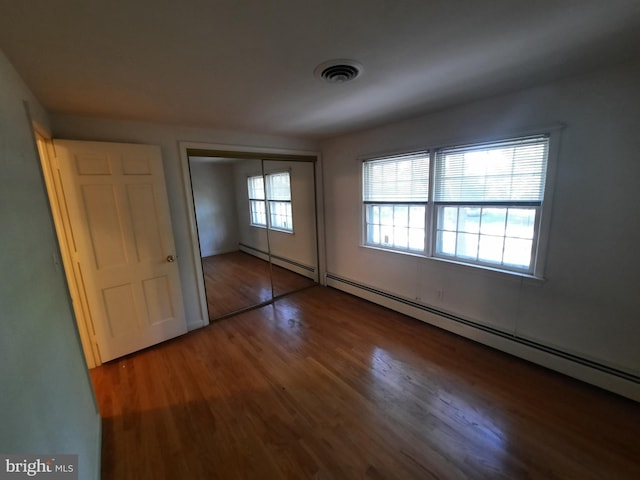 unfurnished bedroom featuring a closet, hardwood / wood-style floors, and a baseboard heating unit