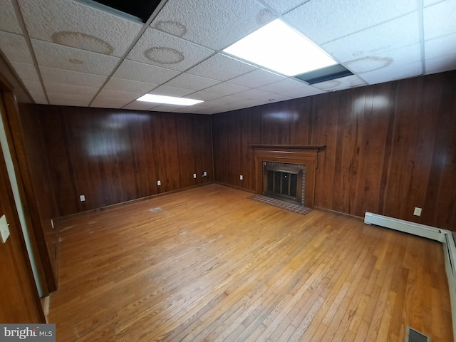 basement with a paneled ceiling, wood walls, light wood-type flooring, and baseboard heating