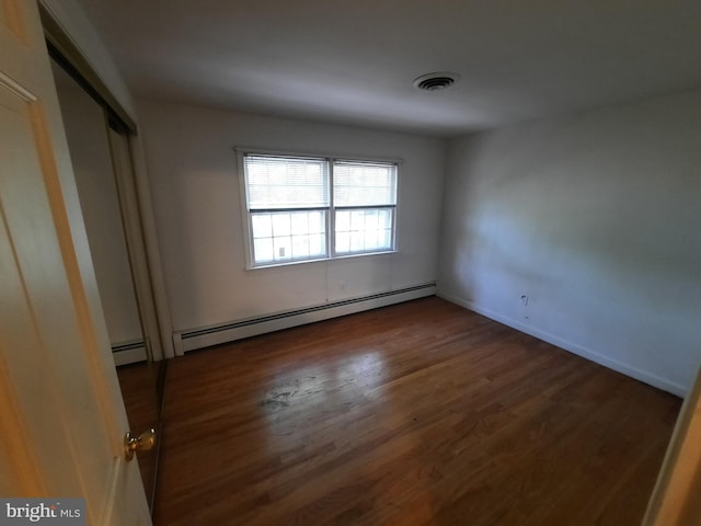 unfurnished bedroom featuring baseboard heating, a closet, and dark wood-type flooring