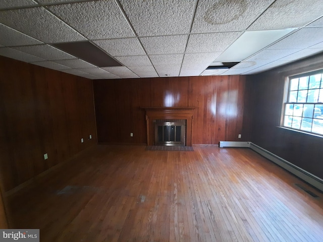 unfurnished living room featuring hardwood / wood-style flooring, a drop ceiling, and wooden walls