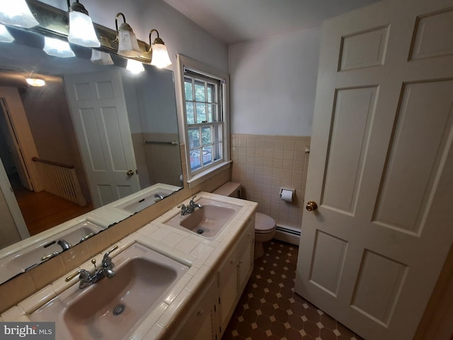 bathroom featuring vanity, toilet, baseboard heating, and tile walls