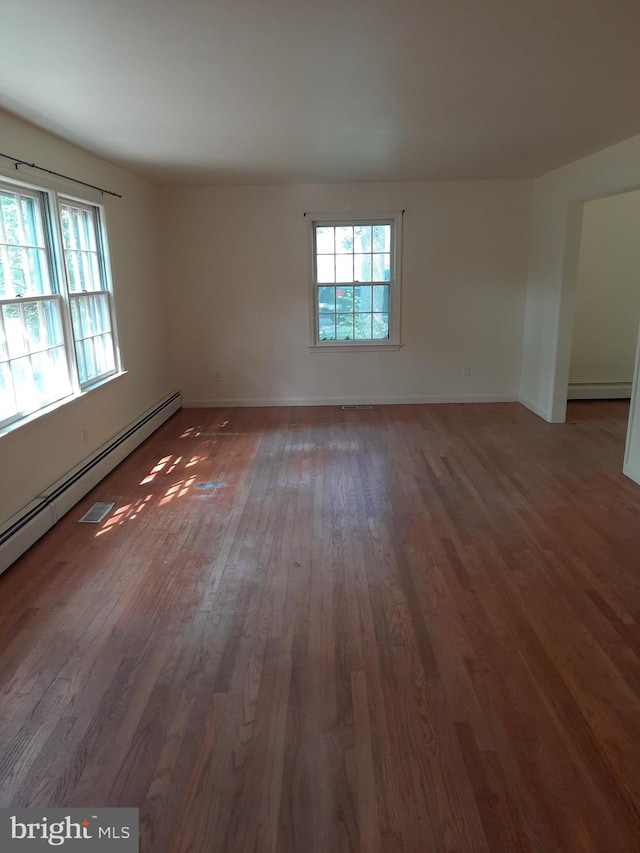 spare room featuring dark hardwood / wood-style flooring, baseboard heating, and a healthy amount of sunlight