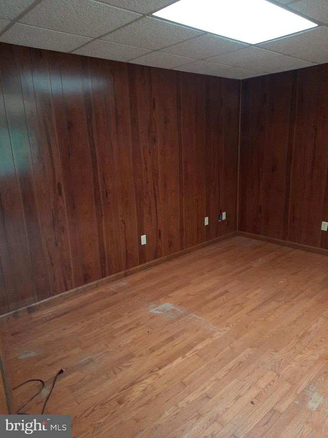 spare room with a paneled ceiling, light hardwood / wood-style floors, and wood walls