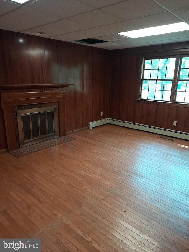 basement featuring a drop ceiling, light hardwood / wood-style flooring, wooden walls, and a brick fireplace