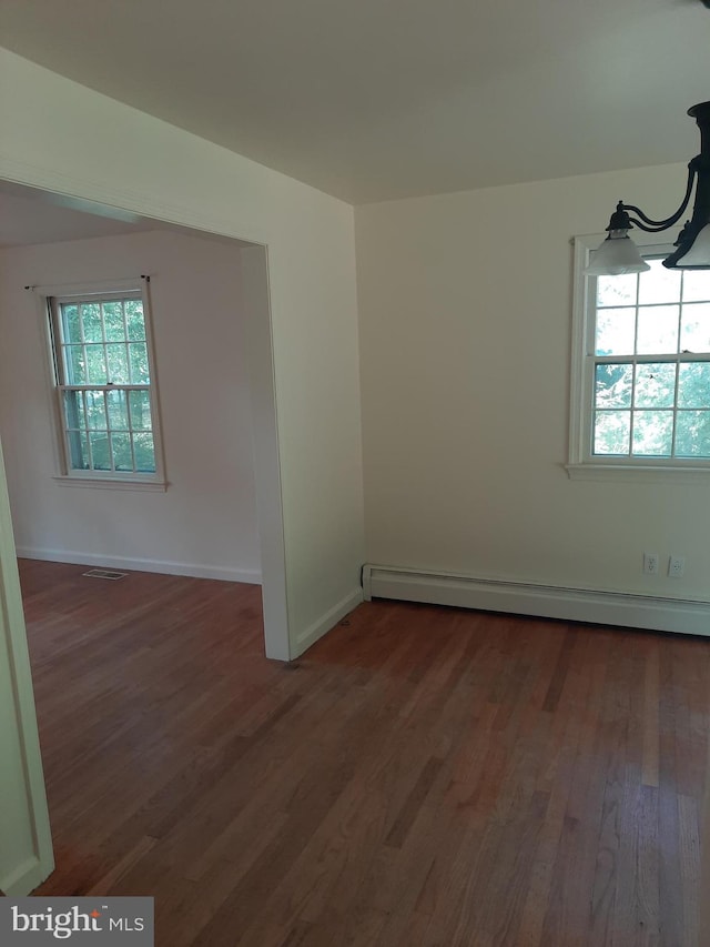 empty room featuring a healthy amount of sunlight, dark wood-type flooring, and a baseboard radiator