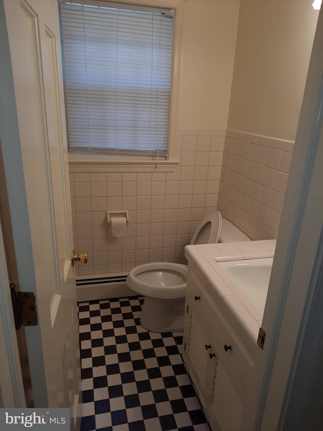 bathroom featuring vanity, toilet, tile walls, and a baseboard heating unit