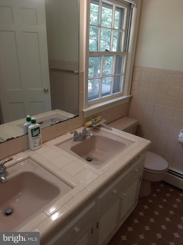 bathroom featuring toilet, vanity, baseboard heating, and tile walls