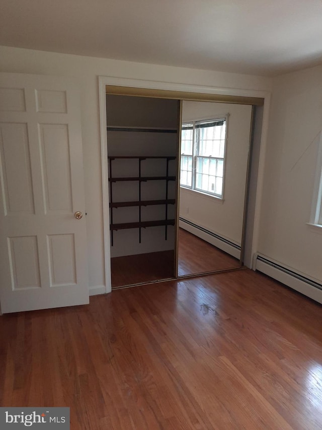 unfurnished bedroom with hardwood / wood-style floors, baseboard heating, and a closet