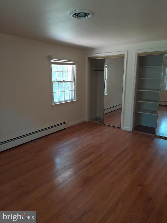 unfurnished bedroom featuring multiple closets, dark hardwood / wood-style flooring, and a baseboard radiator