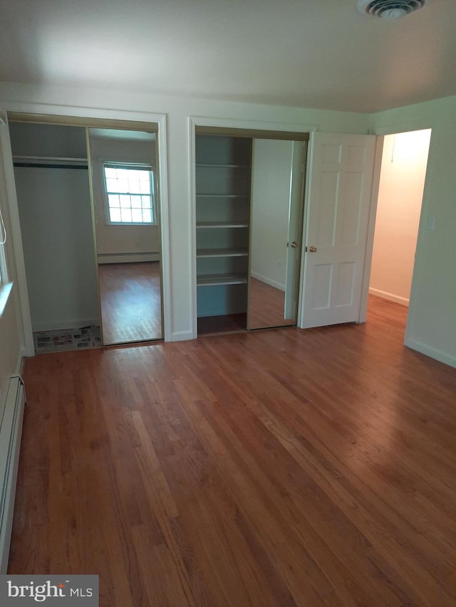 unfurnished bedroom featuring wood-type flooring, multiple closets, and a baseboard heating unit