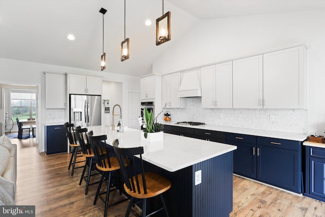 kitchen with custom range hood, stainless steel appliances, a center island with sink, high vaulted ceiling, and white cabinets