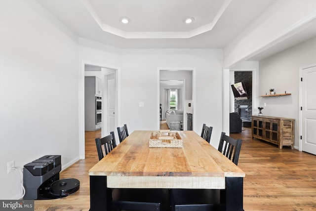 dining area with a fireplace, wood-type flooring, and a raised ceiling