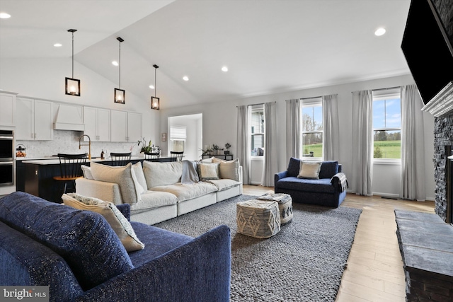 living room featuring high vaulted ceiling, light hardwood / wood-style floors, a stone fireplace, and sink