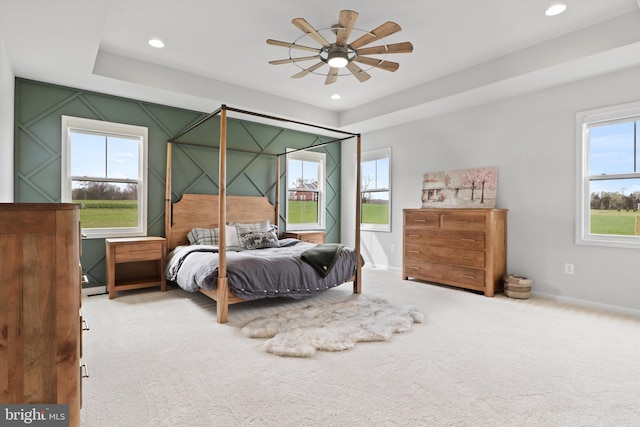 bedroom featuring carpet, ceiling fan, a tray ceiling, and multiple windows