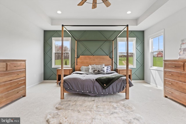 carpeted bedroom with a raised ceiling, multiple windows, and ceiling fan