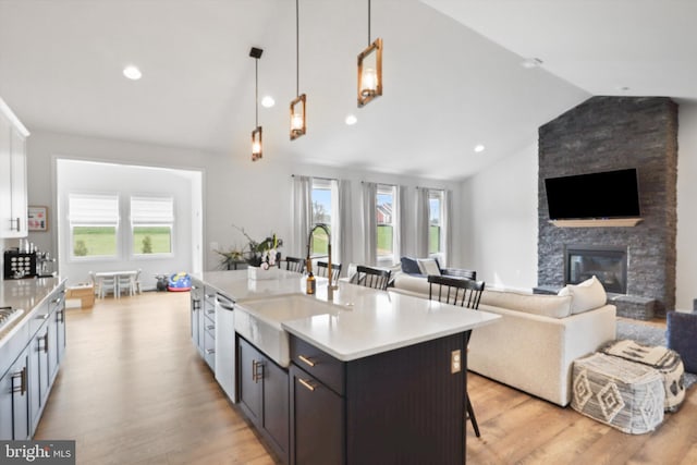 kitchen featuring sink, a stone fireplace, vaulted ceiling, a kitchen island with sink, and a breakfast bar