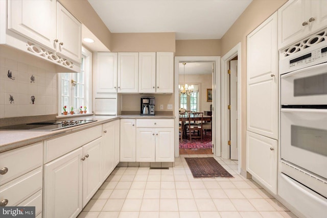 kitchen featuring white cabinets, white double oven, black electric cooktop, and a notable chandelier