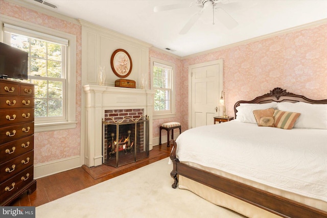 bedroom featuring multiple windows, dark hardwood / wood-style flooring, a brick fireplace, and ceiling fan