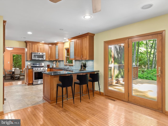 kitchen featuring sink, stainless steel appliances, light hardwood / wood-style flooring, kitchen peninsula, and a kitchen bar