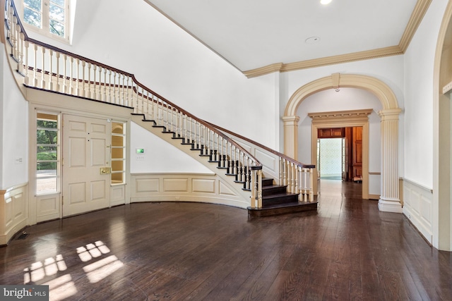 entryway featuring a towering ceiling, dark hardwood / wood-style flooring, ornate columns, and ornamental molding