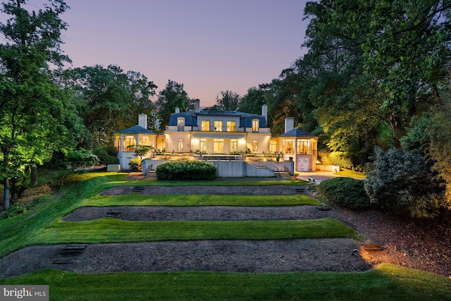 back house at dusk featuring a yard, a balcony, and a swimming pool