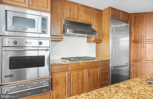 kitchen with built in appliances, light stone countertops, under cabinet range hood, backsplash, and a warming drawer