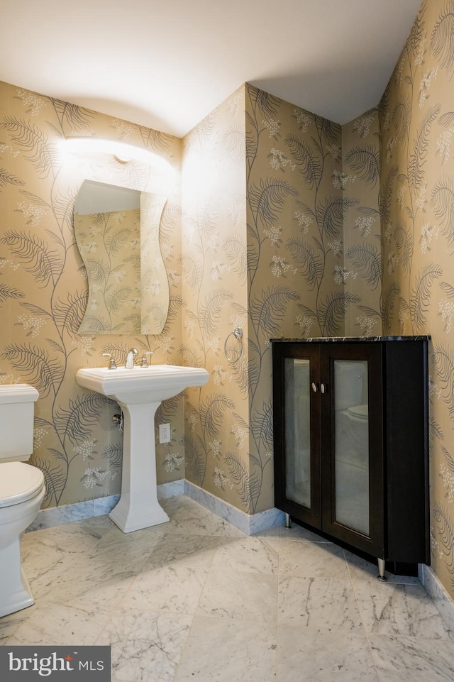 half bathroom with toilet, marble finish floor, and baseboards