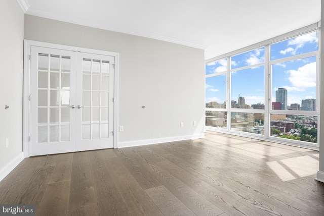 unfurnished room with french doors, a city view, crown molding, expansive windows, and wood finished floors