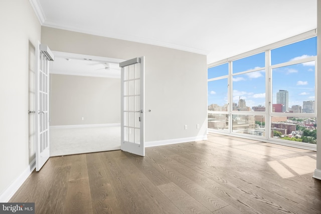 unfurnished room with a city view, wood finished floors, ornamental molding, french doors, and a wall of windows