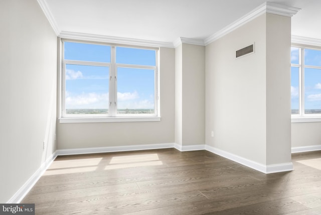 spare room with baseboards, wood finished floors, visible vents, and crown molding