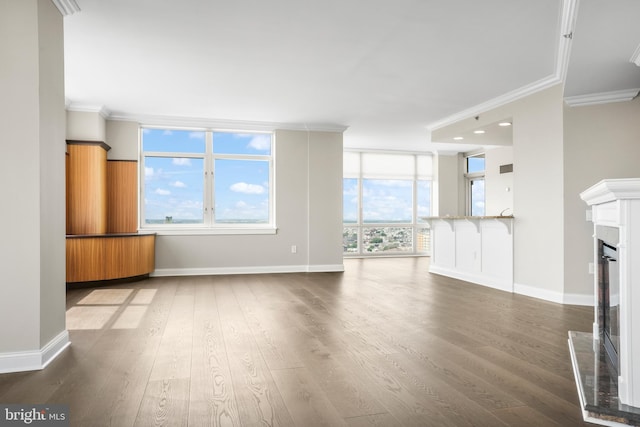 unfurnished living room featuring a fireplace with raised hearth, baseboards, wood finished floors, and crown molding