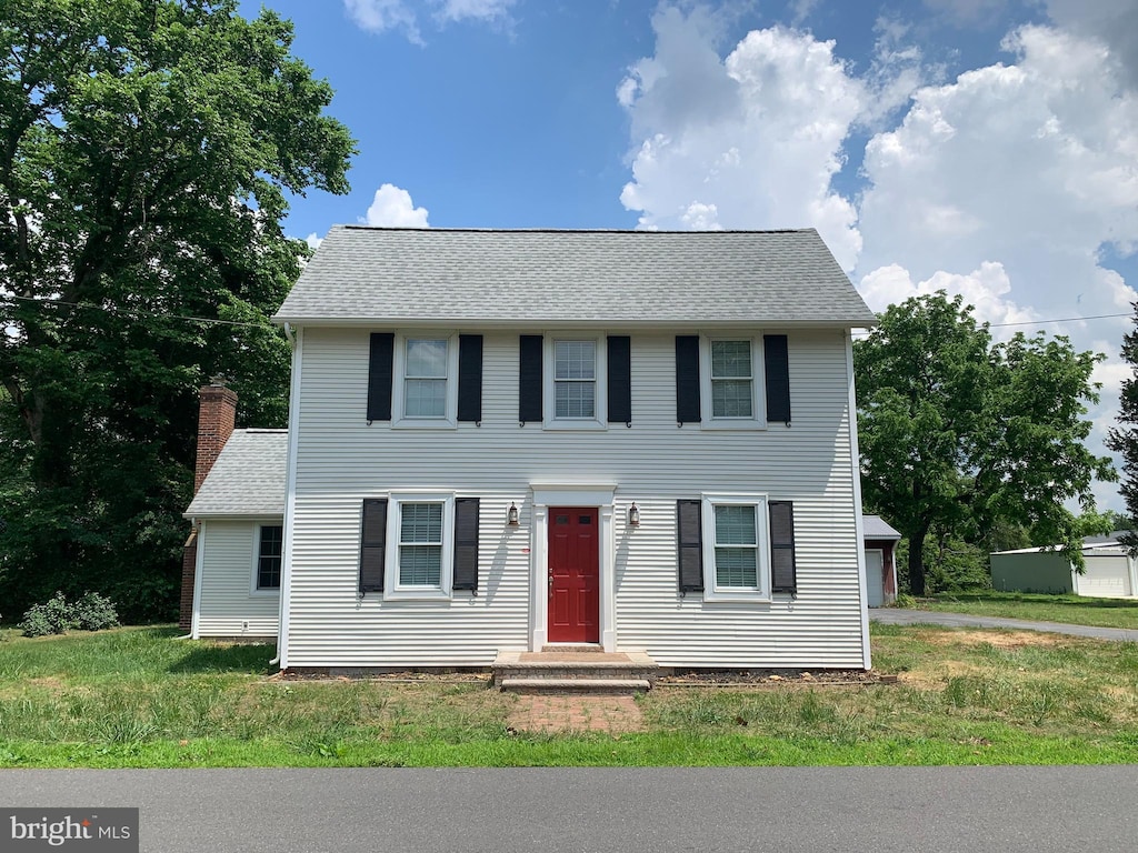 colonial house with a shingled roof, a front yard, and a chimney