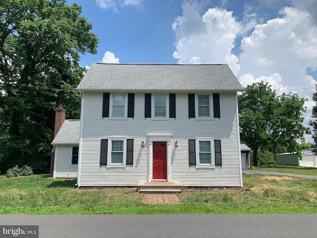 colonial house with a shingled roof, a front yard, and a chimney