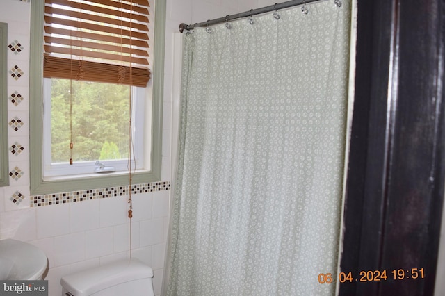 bathroom featuring curtained shower, toilet, and tile walls