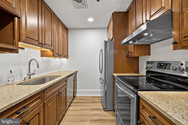 kitchen featuring decorative backsplash, sink, light stone counters, light hardwood / wood-style floors, and appliances with stainless steel finishes