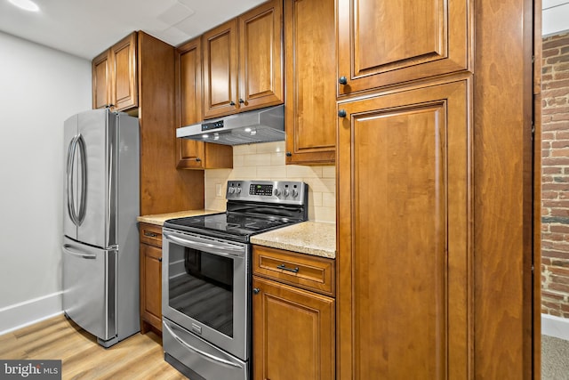 kitchen with light stone counters, light hardwood / wood-style flooring, stainless steel appliances, and backsplash