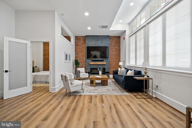 living room featuring brick wall, light wood-type flooring, a brick fireplace, and a towering ceiling