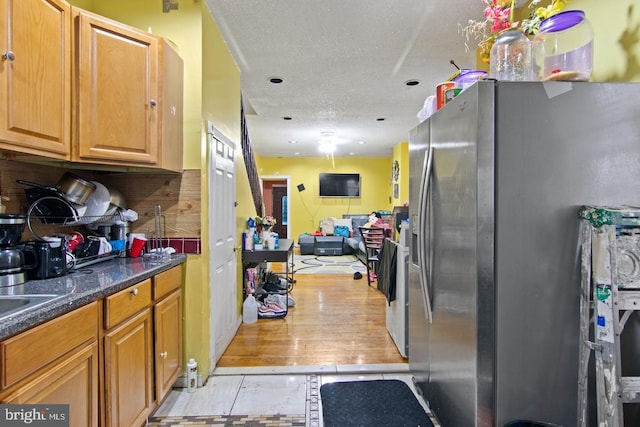 kitchen with a textured ceiling, light wood-type flooring, stainless steel fridge with ice dispenser, and dark stone countertops