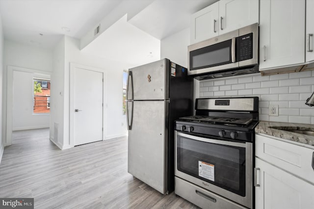 kitchen with appliances with stainless steel finishes, light hardwood / wood-style flooring, tasteful backsplash, light stone countertops, and white cabinetry