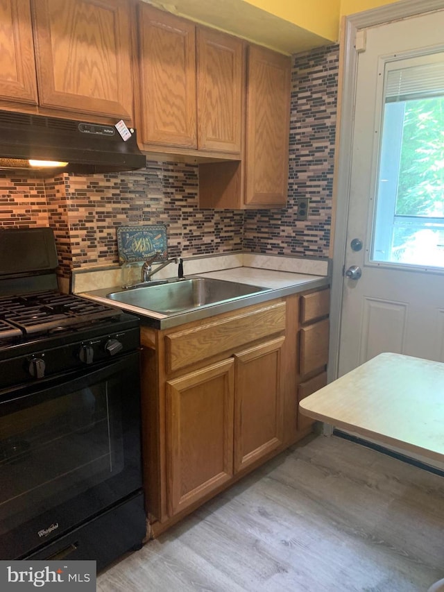 kitchen with black range with gas stovetop, decorative backsplash, sink, and light wood-type flooring