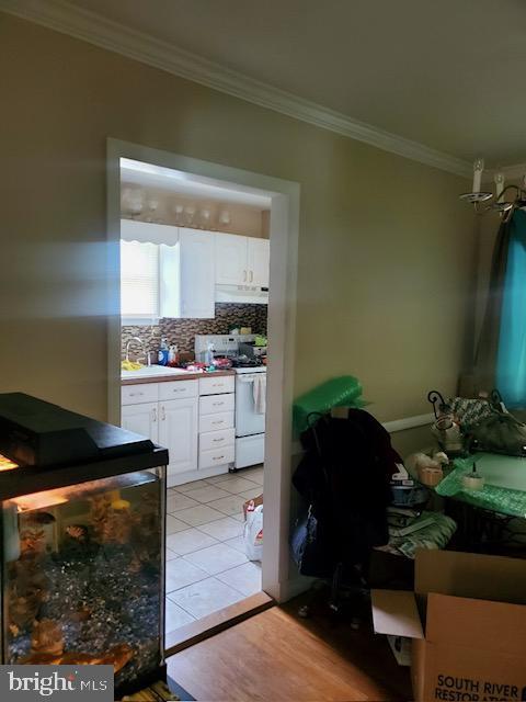 kitchen featuring white range, crown molding, decorative backsplash, light tile patterned floors, and white cabinetry