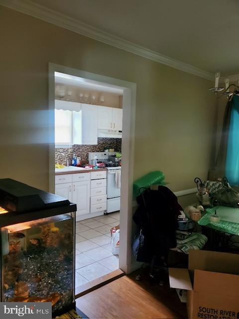 5602 Todd Ave, Baltimore, MD 21206 - kitchen with white stove, under cabinet range hood, ornamental molding, white cabinets, and backsplash