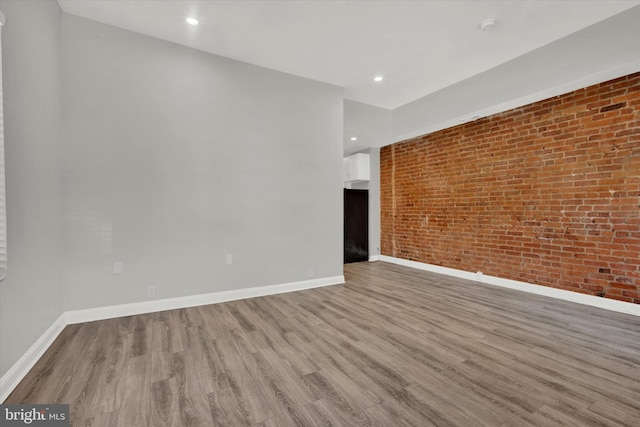 empty room featuring brick wall and light hardwood / wood-style flooring