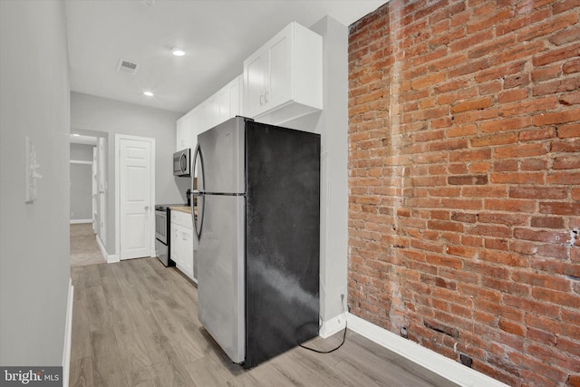 kitchen with white cabinets, light wood-type flooring, brick wall, and appliances with stainless steel finishes