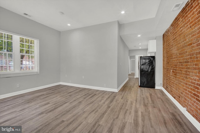 unfurnished living room featuring light hardwood / wood-style flooring and brick wall