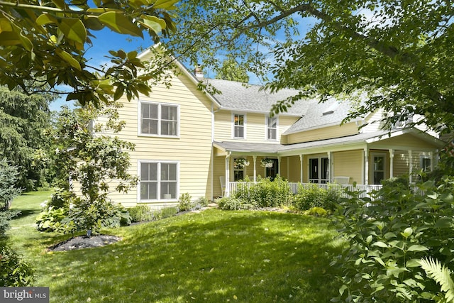 rear view of property featuring a lawn and covered porch