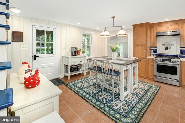 kitchen with backsplash, ornamental molding, light tile patterned floors, stainless steel stove, and hanging light fixtures